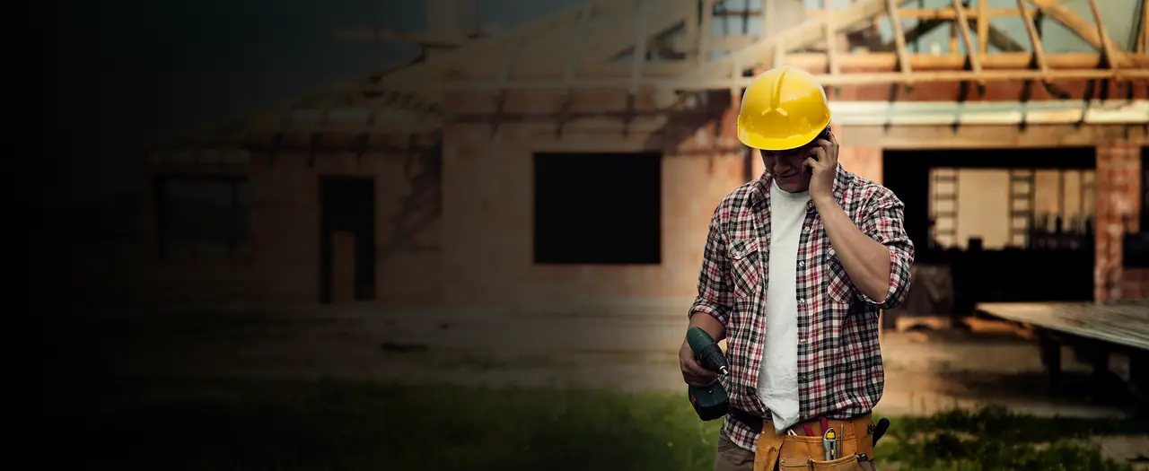 Profissional da construção civil ao telefone em frente a uma casa em obra